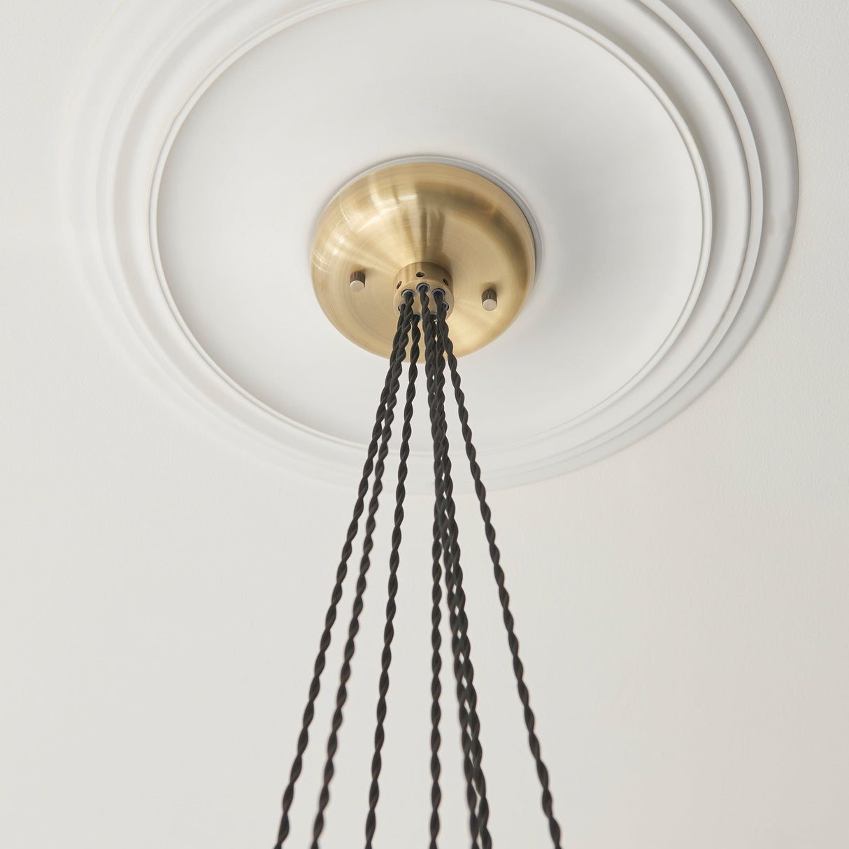Close-up of the Quilbrook Cluster 7 Light Pendant ceiling plate in antique brass, mounted on a circular ceiling rose with twisted black cables descending.