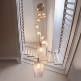 Fennhollow Ribbed Cascade 13 light pendant in antique brass with ribbed clear glass globes falling through a bright stairwell with white shutters.