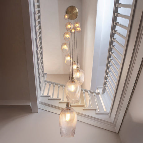 Fennhollow Ribbed Cascade 13 light pendant in antique brass with ribbed clear glass globes falling through a bright stairwell with white shutters.