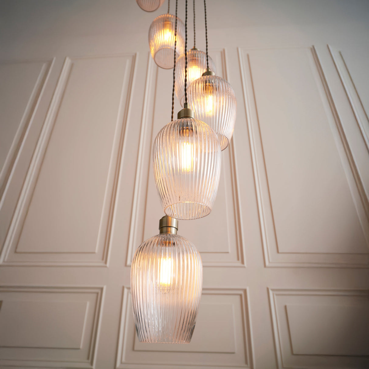 Fennhollow Ribbed Cascade 13 light pendant by Lighting No.1, ribbed clear glass globes on antique brass suspensions against a panelled cream wall.