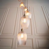 Fennhollow Ribbed Cascade 13 light pendant by Lighting No.1, ribbed clear glass globes on antique brass suspensions against a panelled cream wall.