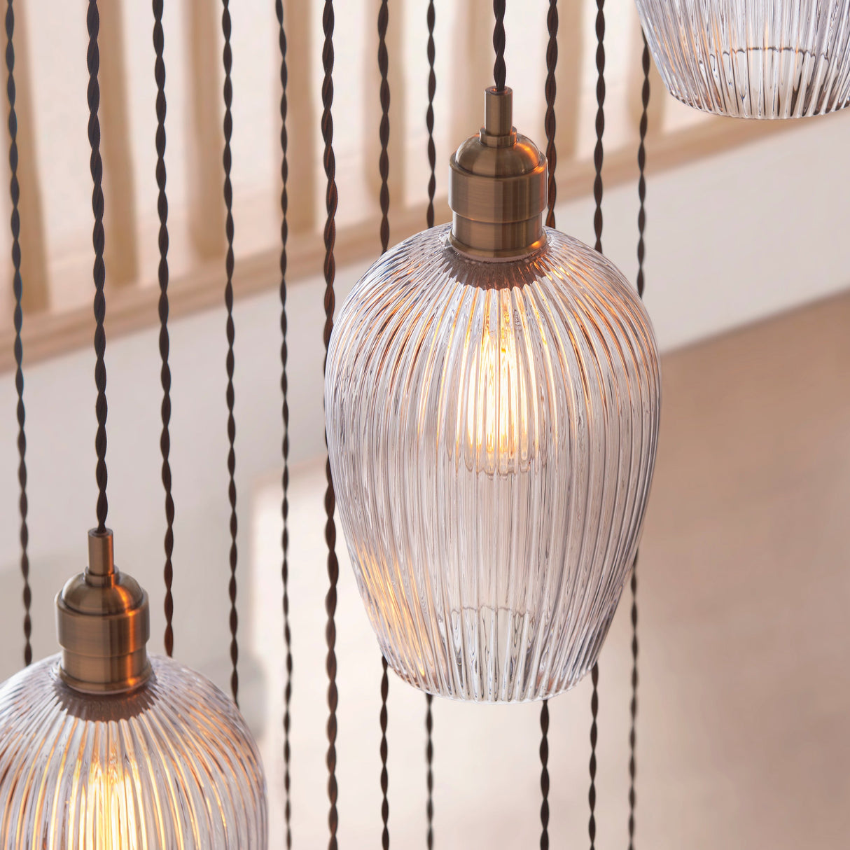 Close-up of Lighting No.1 Fennhollow Ribbed Cascade pendant showing ribbed clear glass globes on antique brass fittings with twisted flex cables in a stairwell.