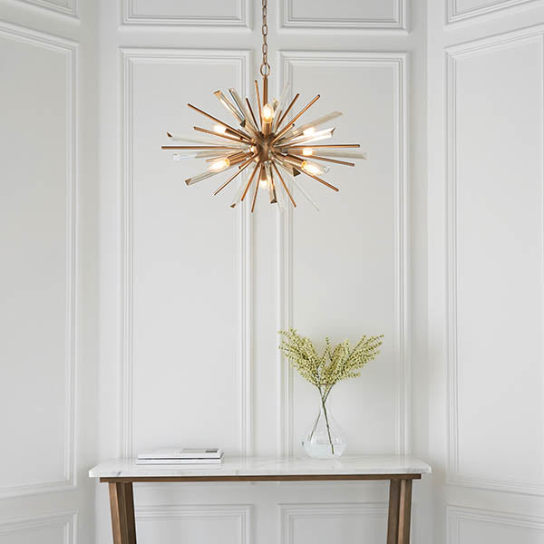 Selmoor Shards 6 Light Pendant in antique brass plated finish with clear glass shards, hung above a marble console table with a vase of foliage.