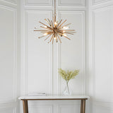 Selmoor Shards 6 Light Pendant in antique brass plated finish with clear glass shards, hung above a marble console table with a vase of foliage.