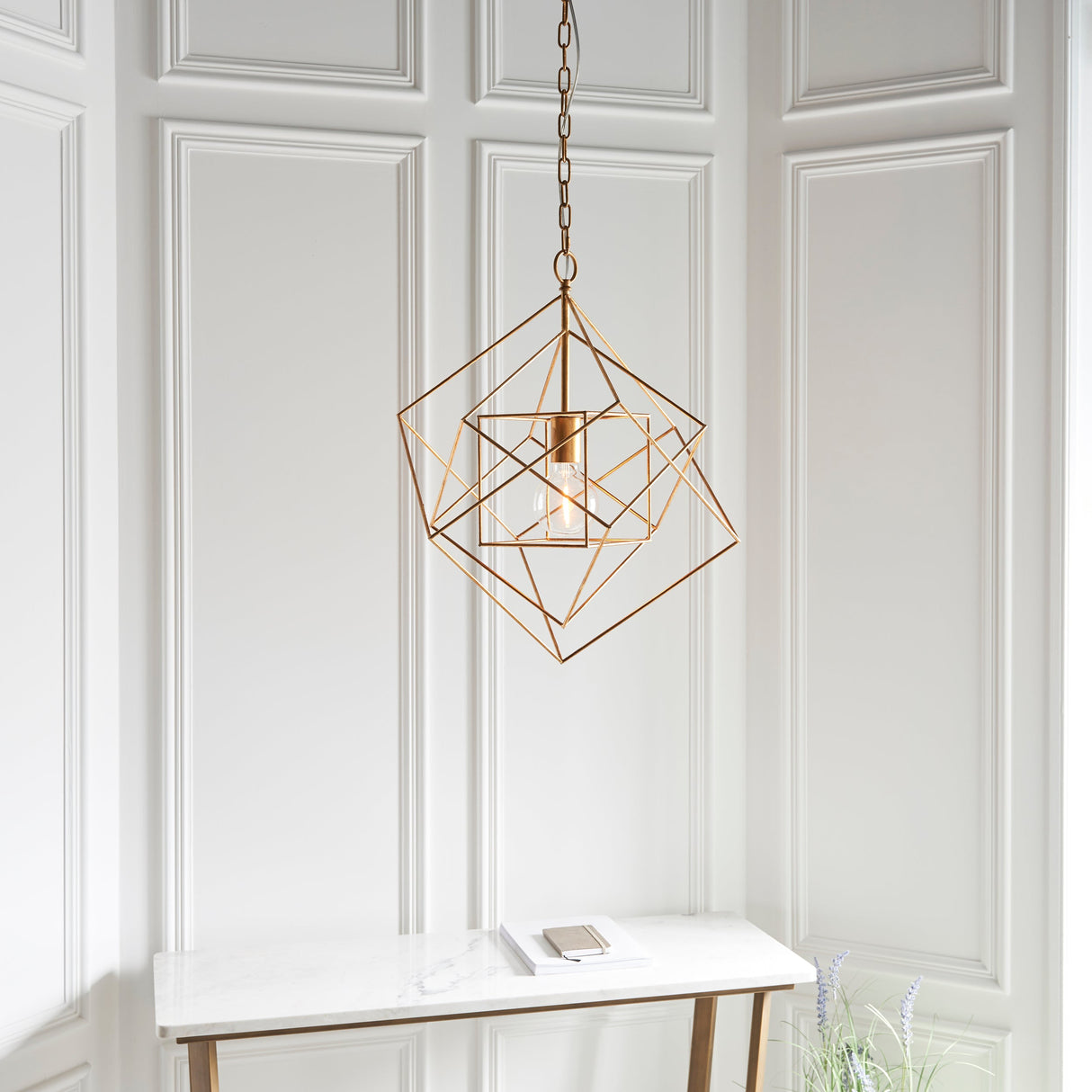 Padgrove Medium Angular Framed Single Pendant in gold leaf by Lighting No.1, hung above a marble console table against white panelled walls.