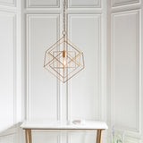Padgrove medium angular framed single pendant in gold leaf by Lighting No.1, hung on a chain above a marble console in a panelled room.