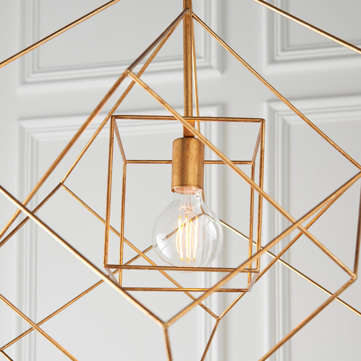 Padgrove medium angular framed single pendant in gold leaf by Lighting No.1, shown close-up with exposed E27 bulb against a panelled wall.