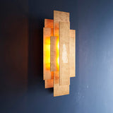 Dunmoor Rectangular Panel 2 Light Wall Light in gold from Lighting No.1, layered metal panels glowing warmly against a dark blue wall.