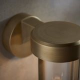 Close-up of Lighting No.1 Yeldmoor die-cast outdoor wall light showing brushed gold circular top, wall bracket, and clear glass cylinder.