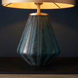 Foxleigh table lamp from Lighting No.1 with a ribbed turquoise glass base and brushed gold fittings beneath a lit gold shade on dark wood.