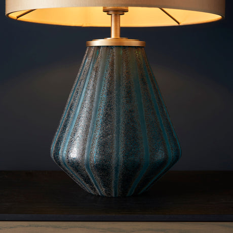Foxleigh table lamp from Lighting No.1 with a ribbed turquoise glass base and brushed gold fittings beneath a lit gold shade on dark wood.