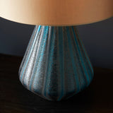 Close-up of the Foxleigh Table Lamp from Lighting No.1, showing its ridged turquoise glass base with textured finish beneath a warm-lit gold shade.