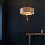 Sparrowmere double hoop 3 light pendant from Lighting No.1 with mink fabric drum shade and gold leaf hoops, hung against a dark blue panelled wall.