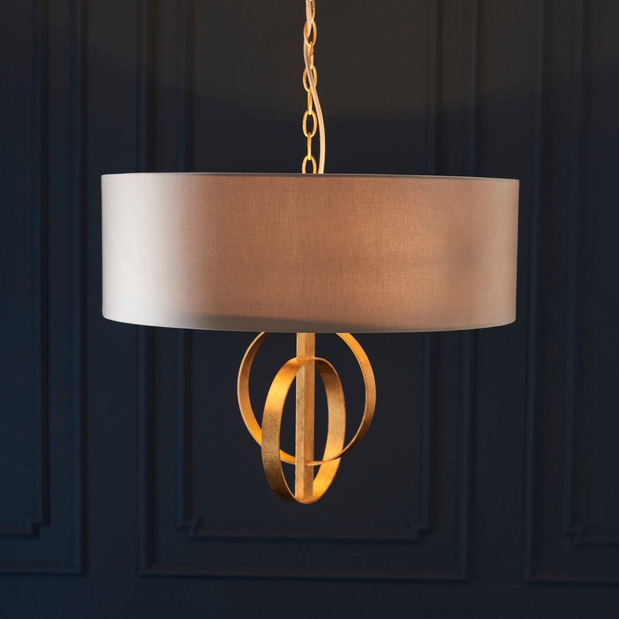 Sparrowmere Double Hoop large 3-light pendant by Lighting No.1 with a mink fabric drum shade and gold leaf hoops, suspended on a chain against dark panelling.