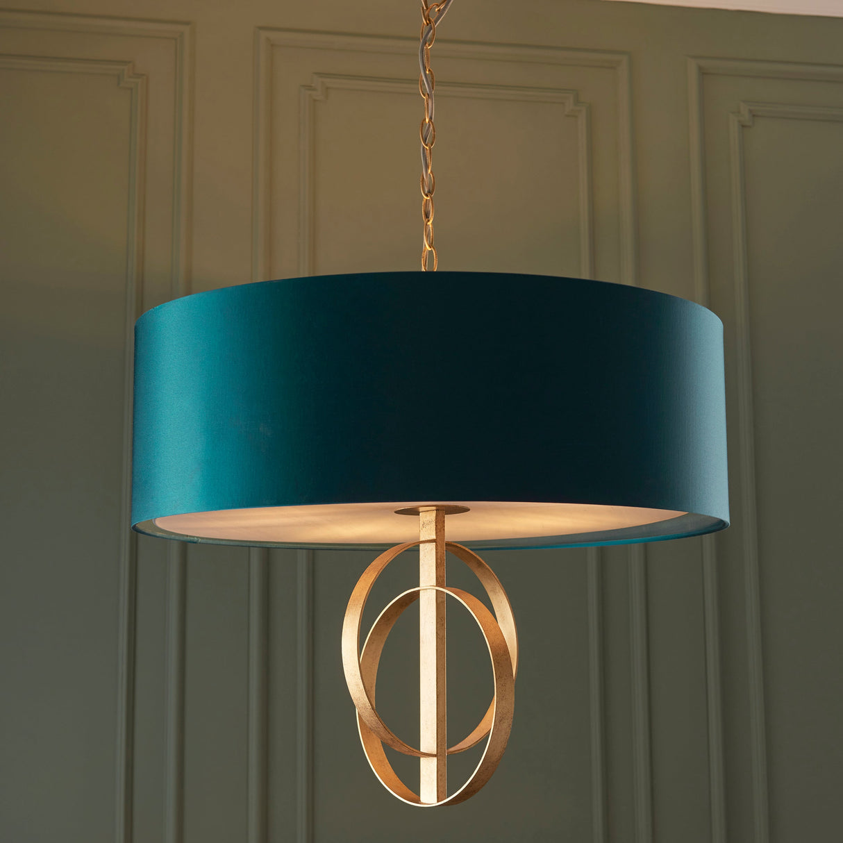 Sparrowmere Double Hoop XL 5 light pendant by Lighting No.1 with teal fabric shade and gold leaf double hoops on a chain, against panelled green wall.