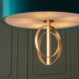 Close-up of Lighting No.1 Sparrowmere Double Hoop XL pendant showing gold leaf interlocking hoops beneath a teal fabric shade against a green panelled wall.