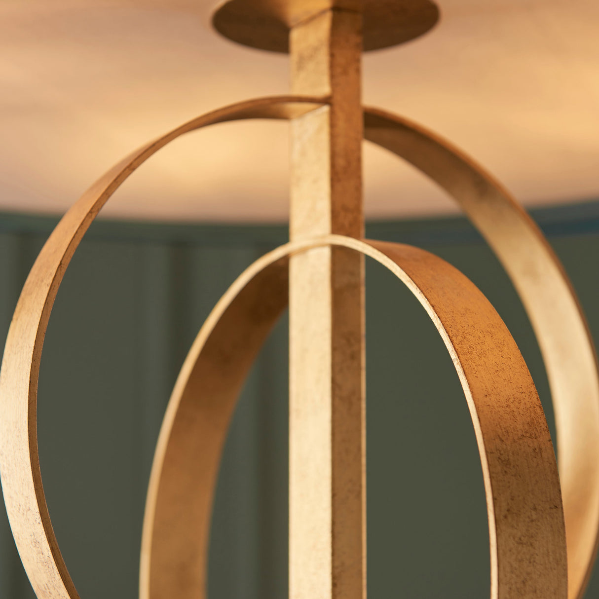 Close-up of the Sparrowmere Double Hoop XL pendant by Lighting No.1, showing two gold leaf metal hoops and ceiling plate against a teal wall.