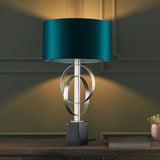 Sparrowmere Double Hoop table lamp with silver leaf interlocking hoops, teal fabric drum shade and dark square base on a wooden console.