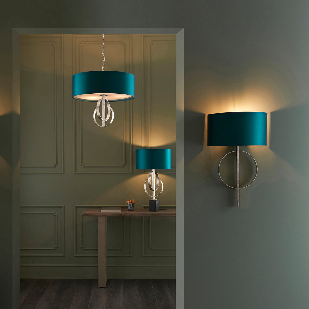 Sparrowmere double hoop table lamp with silver leaf metal frame and teal drum shade on a console, beside a matching pendant and wall light.