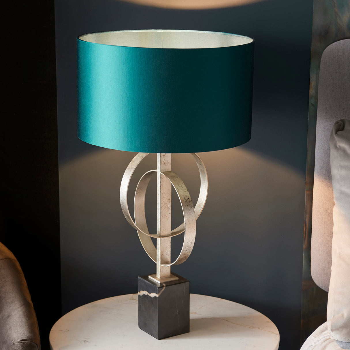 Sparrowmere Double Hoop table lamp from Lighting No.1 with teal drum shade, silver leaf metal hoops and marble base on a side table.