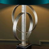 Close-up of the Sparrowmere Double Hoop table lamp by Lighting No.1, showing interlocking silver leaf metal hoops beneath a teal fabric shade.