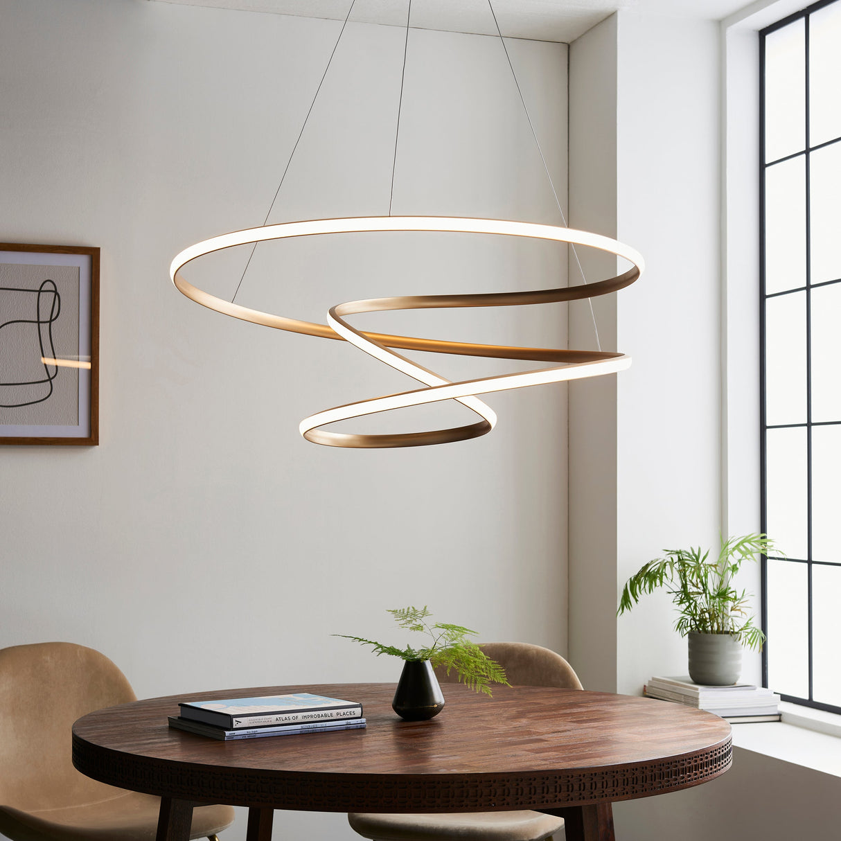 Tolmere Spiral Large Pendant by Lighting No.1 in a natural metal finish, coiled LED ribbon suspended above a round wooden dining table.