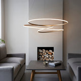 Tolmere Spiral Grand Pendant in natural metal finish, illuminated above a concrete coffee table between grey sofas beside a log-filled fireplace.