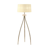 The Loewe 3 Light Floor Lamp features a brass finish with three slender gold legs, a decorative glass accent near the top, and a wide cream fabric shade.
