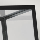 In the image, there is a close-up of the Lofoten Outdoor 1 Light Wall Light - Black, featuring its IP44-rated glass panel with a black frame intersected by sleek metal lines. The corner focus highlights the reflections and transparency of its modern design against a light gray background.