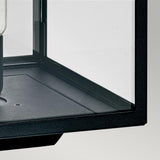 Close-up view of a corner of a display case with a black frame, offering a glimpse of an item inside. The clear glass panels highlight the minimalistic and modern design, similar to the sophisticated outdoor lighting displays such as the Lofoten 1 Light Pedestal - Black, set against a backdrop of neutral tones.