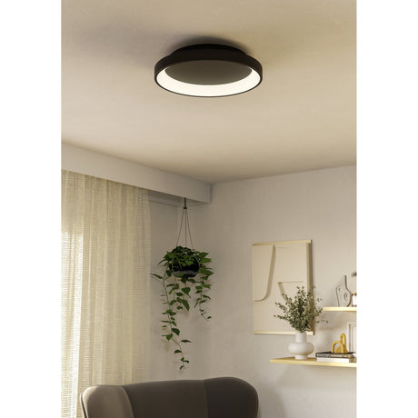 Loretello 35cm LED flush ceiling light in black with a white diffuser ring, mounted on a living room ceiling above a hanging plant and armchair.
