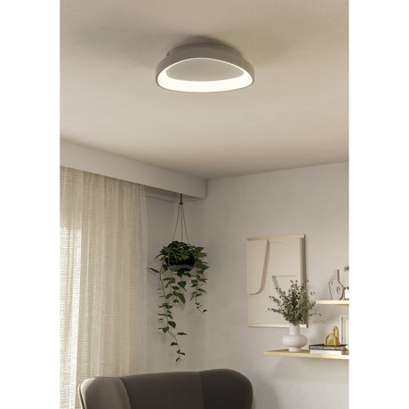 Loretello LED Flush Ceiling Light 35cm in white, round low-profile fixture with recessed diffuser, shown installed on a living room ceiling above a hanging plant and seating area.