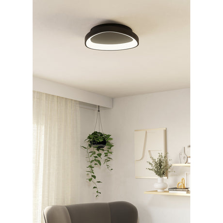 Loretello LED flush ceiling light in black, 35cm rounded design with white diffuser ring, shown mounted on a living room ceiling above a sofa and hanging plant.