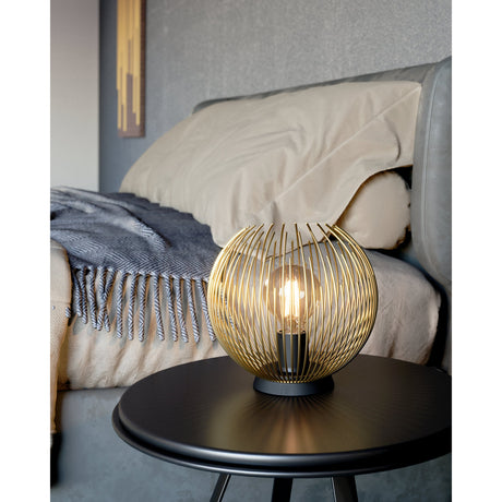 Losmora table lamp with a spherical gold steel rod cage and round black base, lit by an E27 bulb on a black bedside table in a bedroom setting.