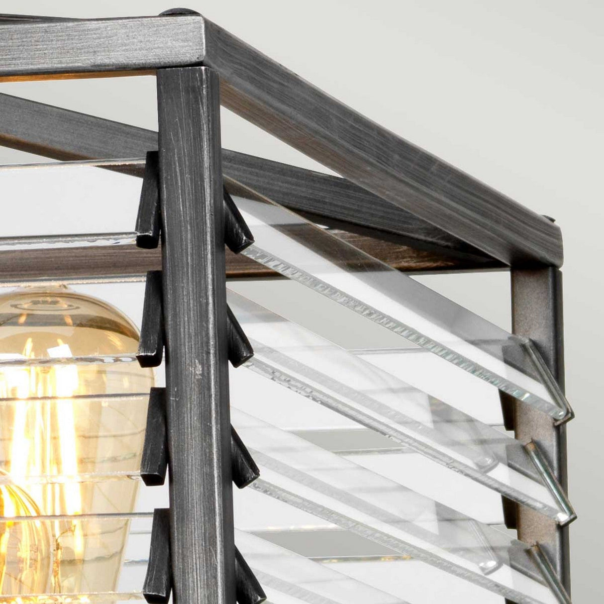 Close-up of the Louvre 6 Light Chandelier, featuring a graphite finish with multiple clear glass panels. Inside, a glowing bulb creates a warm ambiance that exudes vintage charm.