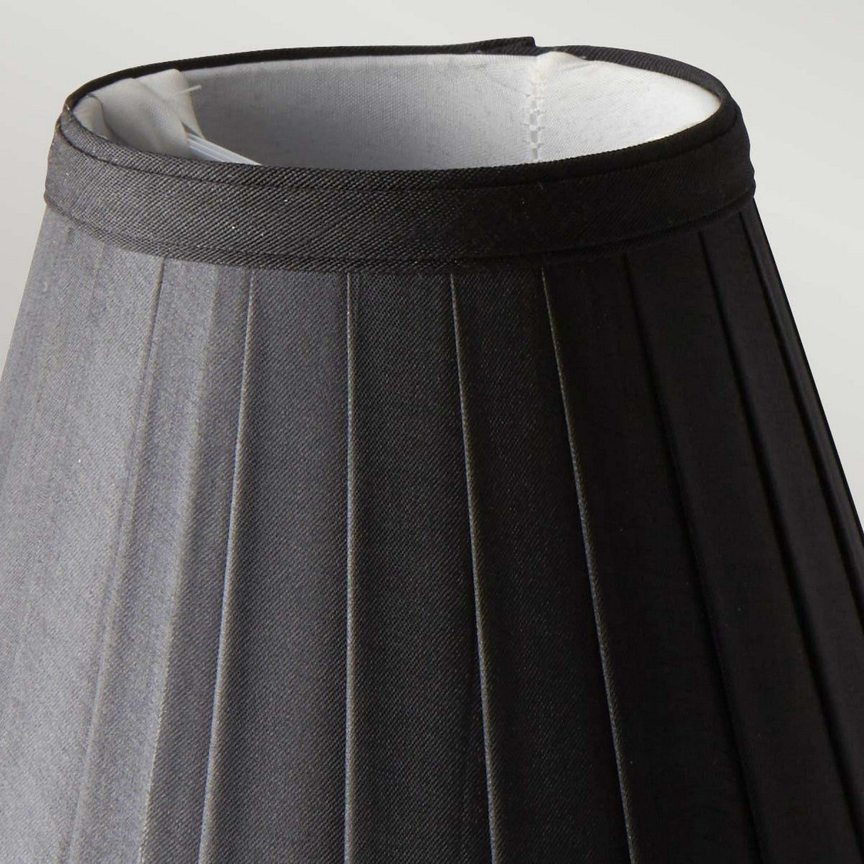 The Clip Shades Pleated Black Candle Shade features a close-up of its design, showcasing a slightly textured black exterior and a white interior. Set against a neutral background, this fabric lampshade is expertly crafted for use as a clip-on shade for candle bulb lighting fixtures.