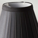 The Clip Shades Pleated Black Candle Shade features a close-up of its design, showcasing a slightly textured black exterior and a white interior. Set against a neutral background, this fabric lampshade is expertly crafted for use as a clip-on shade for candle bulb lighting fixtures.
