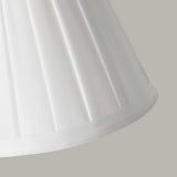 A close-up of the Clip Shades Pleated White Candle Shade crafted from pleated polycotton fabric against a gray background. The fabric folds create a vertical pattern, giving the lighting fixture a classic, elegant appearance.