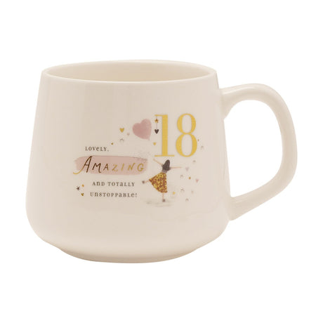 Cream stoneware mug with a gold "18", pink heart balloon, gold-script "Amazing" text, and an illustrated figure in a gold skirt, set on a plain white background.