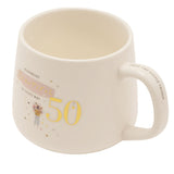 White stoneware birthday mug with gold "50" and "Blooming Beautiful in every way" text, pink brushstroke accent, and a floral figure illustration, shown on a plain white background.