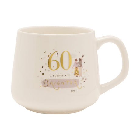 White stoneware mug with glossy finish and gold "60" birthday design, featuring hearts, stars, two illustrated figures, and "a bolder and brighter you" text, shown on a plain white background.
