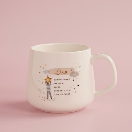 White stoneware "Dad" mug with pink wash, gold star and striped figure illustration, printed strong, kind and fearless message, set against a plain pink background.