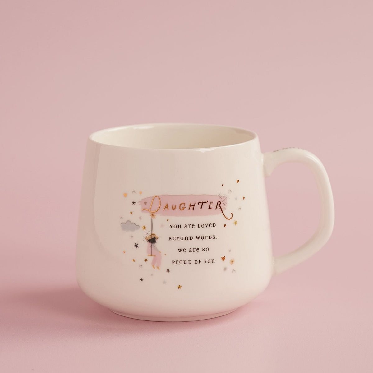 White stoneware mug with pink background, featuring "Daughter" in gold script, a loving message, a figure on a swing, cloud, and scattered gold and pink stars.