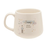 Cream stoneware mug with gold "Daddy" script, "you are my hero!" text, and an illustration of a man holding a balloon amid pastel clouds, stars, and gold hearts, shown on a white background.
