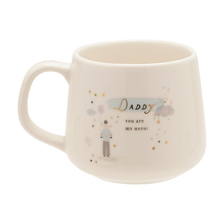 Cream stoneware mug with gold "Daddy" script, "you are my hero!" text, and an illustration of a man holding a balloon amid pastel clouds, stars, and gold hearts, shown on a white background.