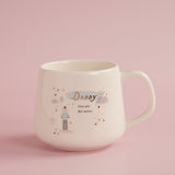 Cream stoneware mug with C-handle, printed Daddy you are my hero in gold script with dad carrying child, balloon, clouds and gold hearts, on pink background.