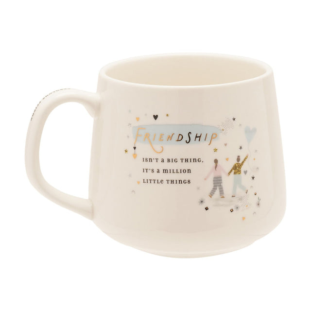 White stoneware mug with C-handle, printed with "Friendship isn't a big thing, it's a million little things" in gold script, featuring two figures and a heart balloon on a plain white background.
