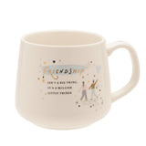 White stoneware mug with C-handle, printed with "Friendship" in gold over a blue brushstroke and two figures with a heart balloon, shown on a plain white background.