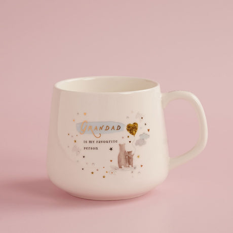 Cream stoneware mug with "Grandad is my favourite person" in gold script, featuring two bears beside a gold heart balloon and stars, shown on a pink background.