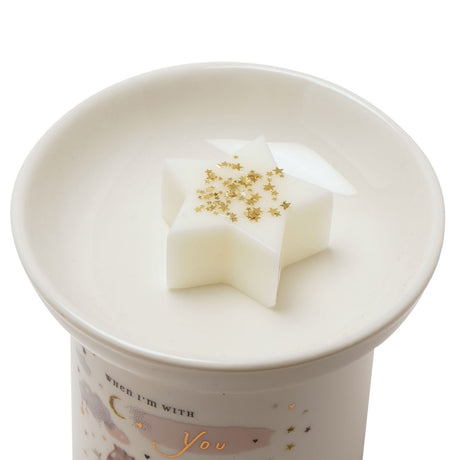 Close-up of the Feels Like Home Ceramic Wax Melt Burner's round white dish holding a star-shaped white wax melt topped with gold star glitter, set against a plain white background.